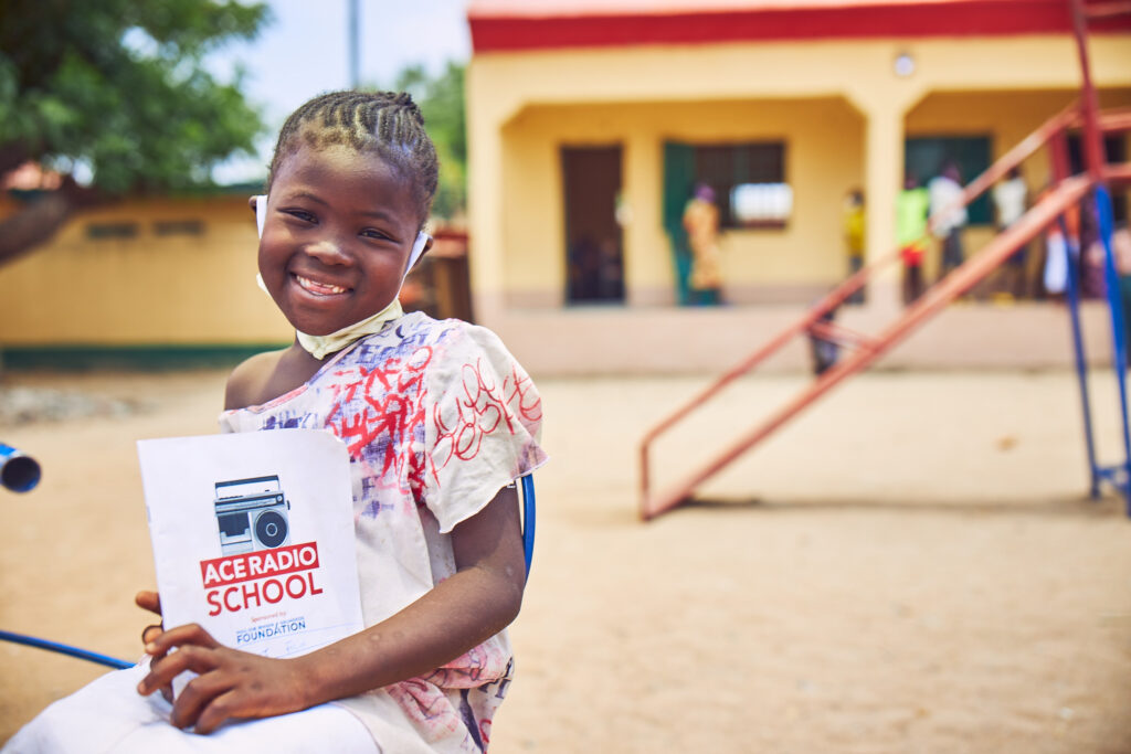 Girl with school material in front of playground and school building