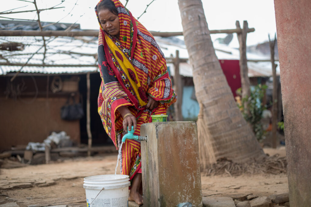 Sukanthi tapper vand fra drikkevandssystemet i hendes landsby Rudhapadar i delstaten Odisha.