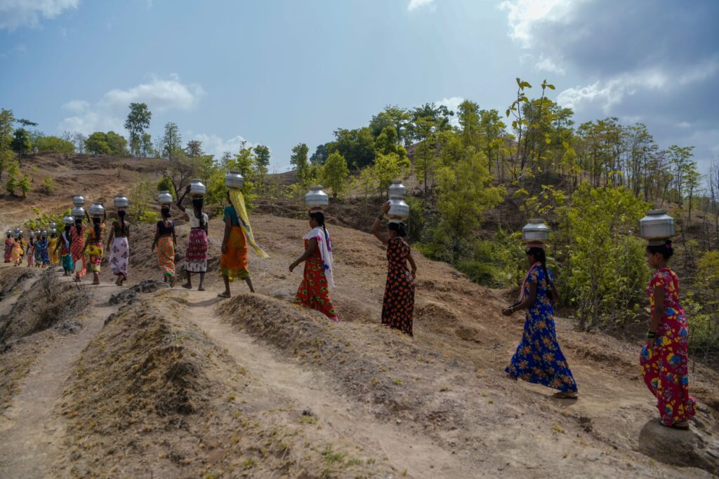 Women carrying water across a dry hilly landscape
