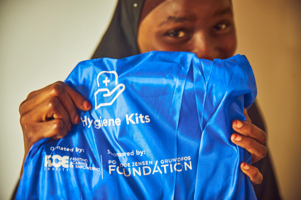 One lady holding up a blue bag with a hygiene kit. in front of her face