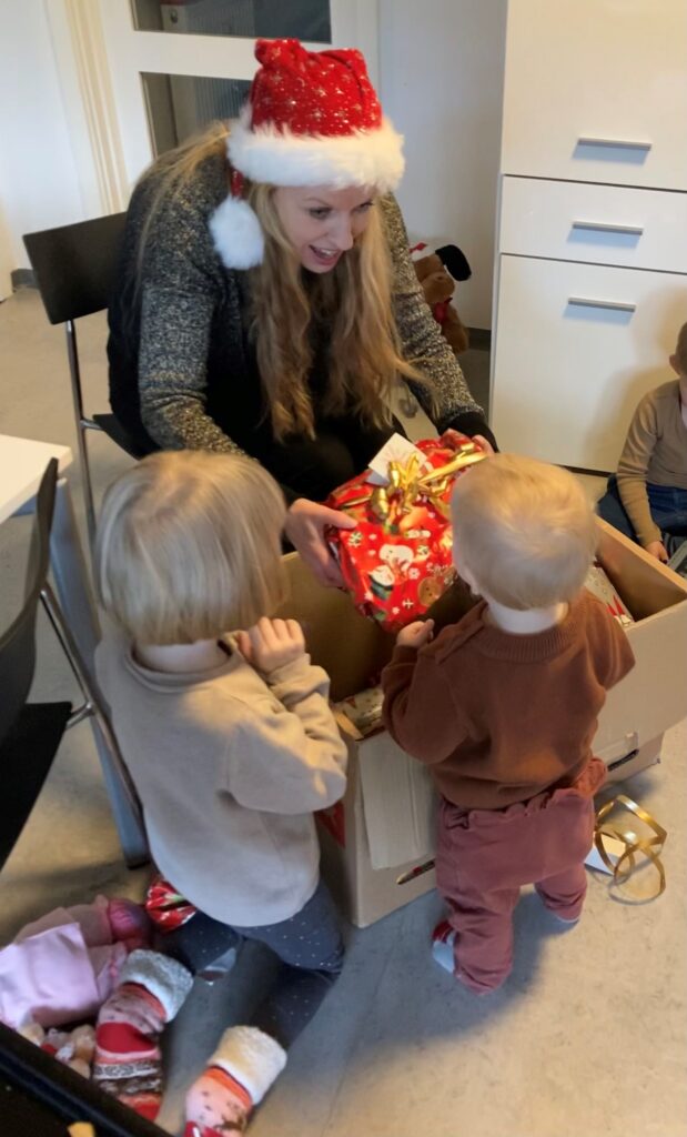 Kvinde i nissehue deler gaver ud til to mindre børn.